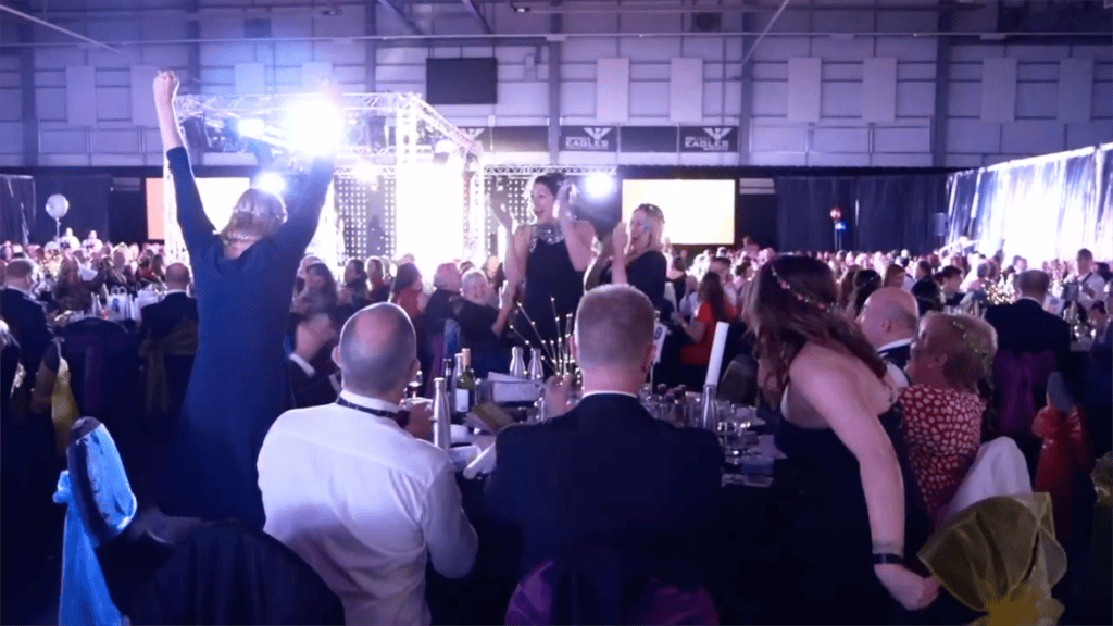 Packed room of guests cheering at an awards evening, filmed for an event promo video