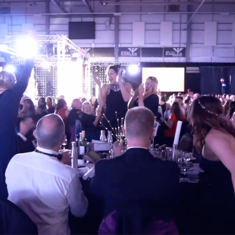 Packed room of guests cheering at an awards evening, filmed for an event promo video