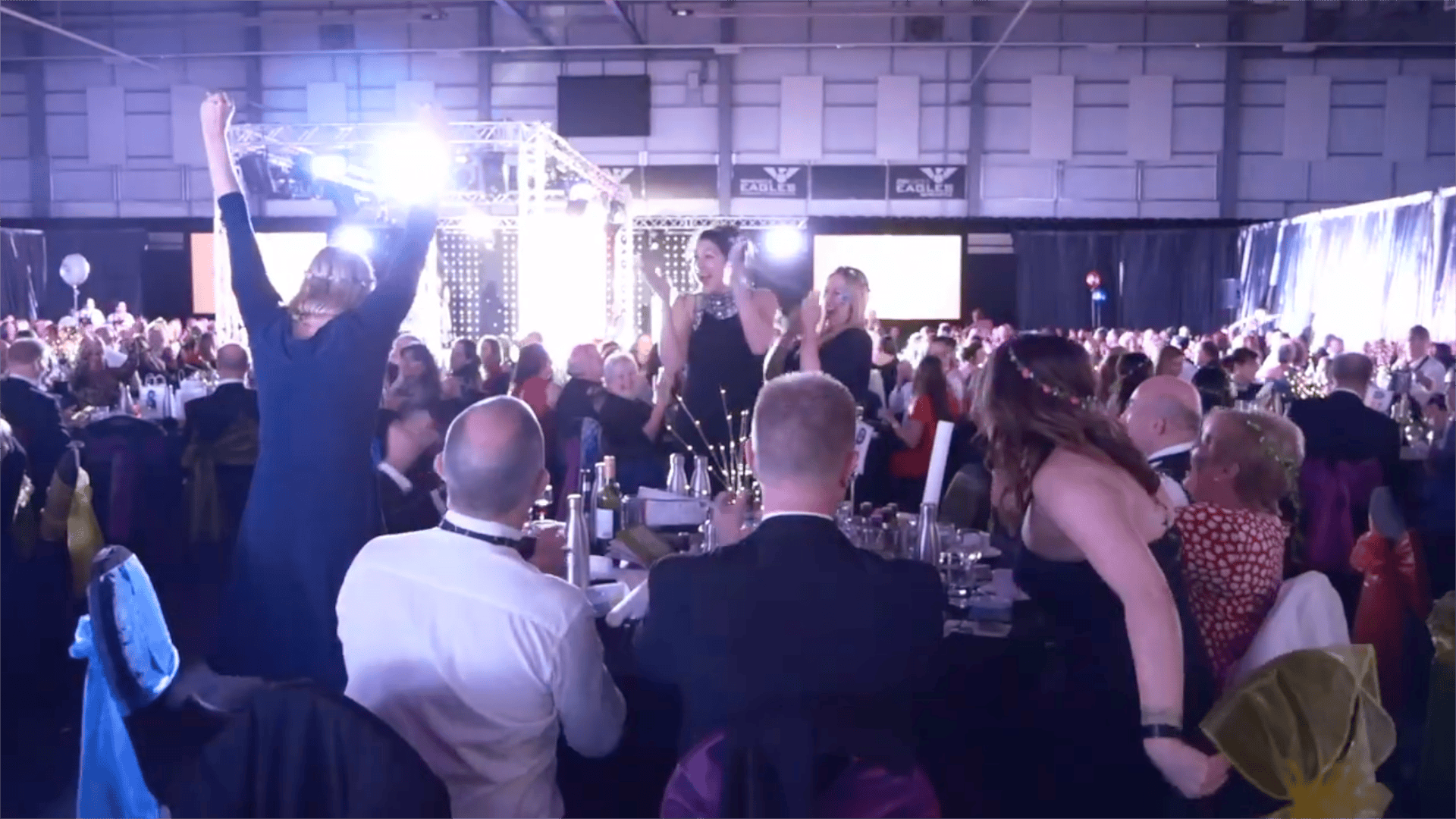 Packed room of guests cheering at an awards evening, filmed for an event promo video