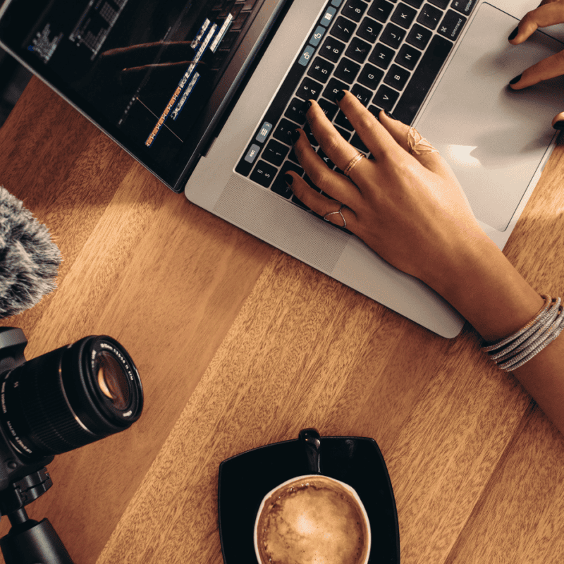Hands typing on a laptop beside a camera and microphone during video editing
